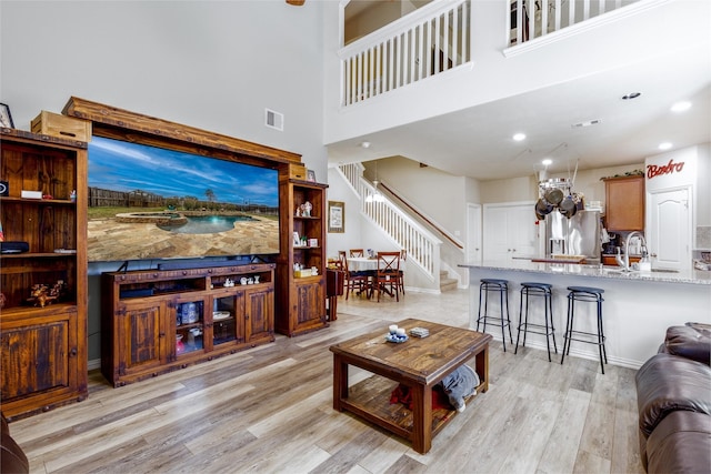 living area featuring stairway, visible vents, a high ceiling, light wood-style flooring, and recessed lighting