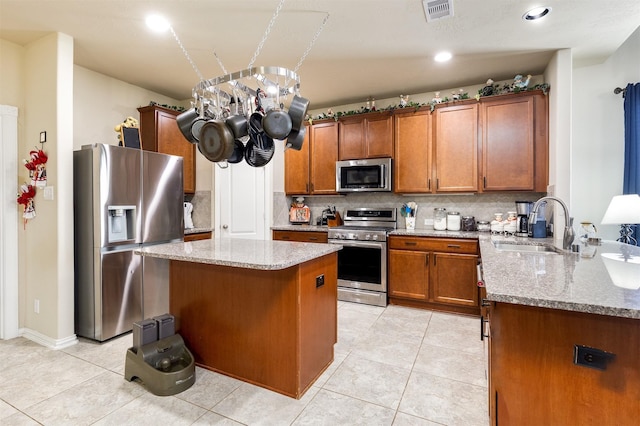 kitchen featuring brown cabinetry, light stone countertops, a sink, decorative backsplash, and stainless steel appliances