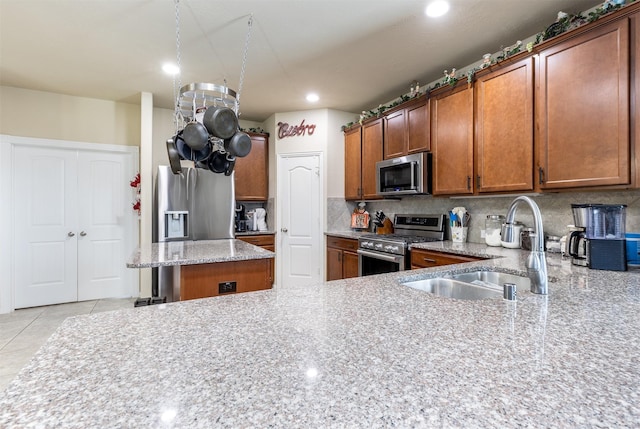 kitchen featuring light stone countertops, a sink, appliances with stainless steel finishes, brown cabinets, and backsplash