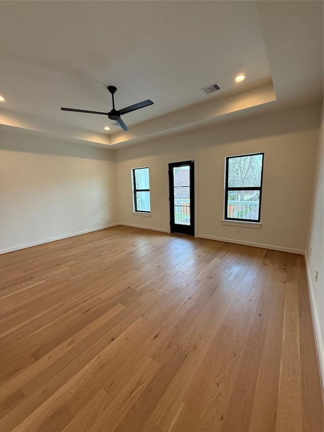 unfurnished room featuring visible vents, a tray ceiling, light wood-style flooring, and baseboards