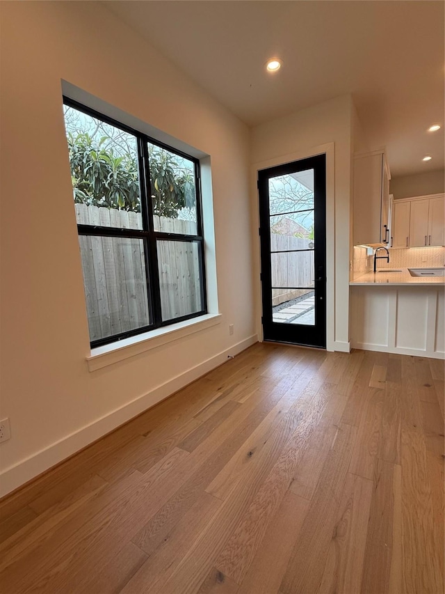 doorway with baseboards, recessed lighting, a sink, and light wood-style floors