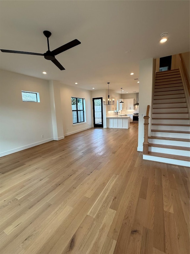 unfurnished living room with recessed lighting, stairway, light wood-style floors, a ceiling fan, and baseboards