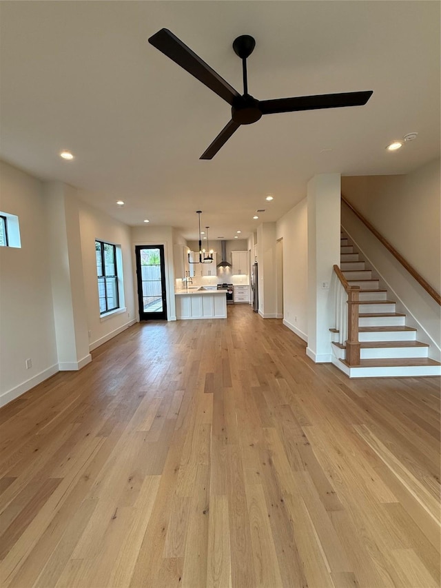 unfurnished living room with light wood-style floors, stairway, a ceiling fan, and recessed lighting