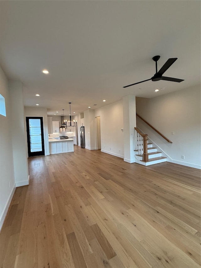 unfurnished living room with light wood finished floors, stairs, baseboards, and recessed lighting