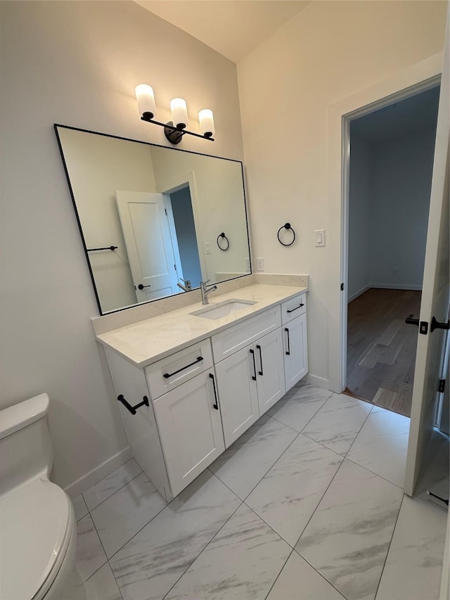 bathroom featuring toilet, marble finish floor, baseboards, and vanity