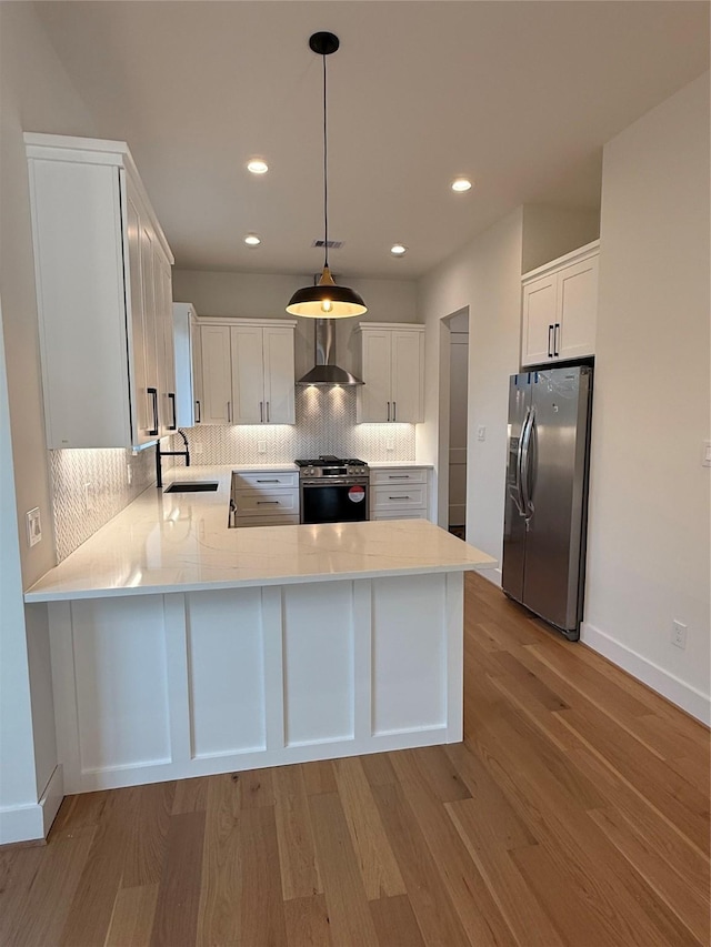 kitchen with stainless steel appliances, a peninsula, a sink, wall chimney range hood, and light wood-type flooring