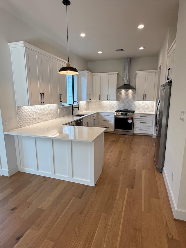 kitchen with stainless steel appliances, a peninsula, a sink, visible vents, and wall chimney range hood