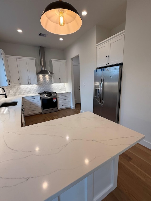 kitchen featuring visible vents, appliances with stainless steel finishes, light stone countertops, wall chimney range hood, and a sink