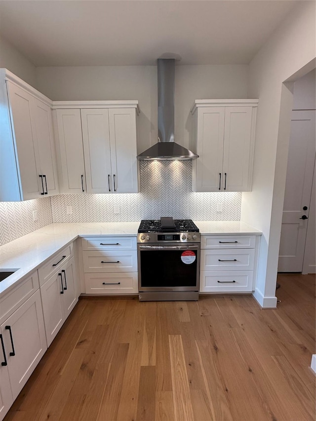 kitchen with light wood-style floors, light countertops, wall chimney range hood, stainless steel range with gas cooktop, and white cabinetry