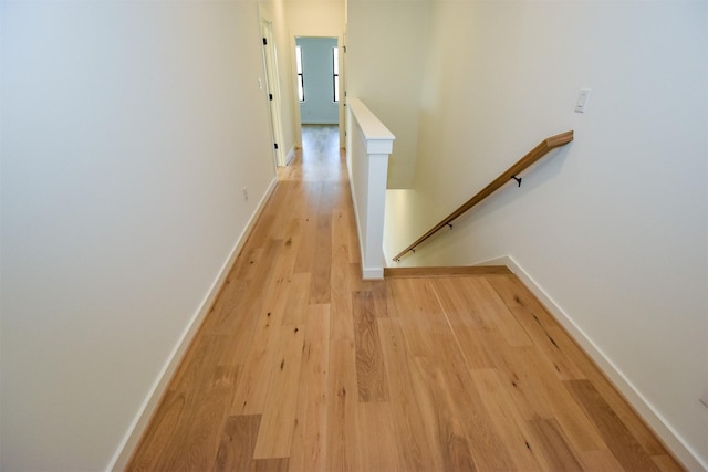 corridor with light wood-style flooring, baseboards, and an upstairs landing