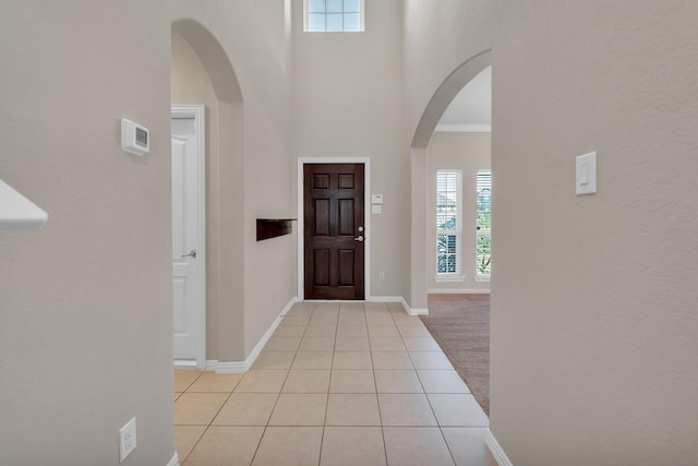 foyer featuring light tile patterned floors, baseboards, arched walkways, and a healthy amount of sunlight