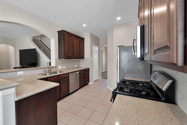 kitchen featuring backsplash, appliances with stainless steel finishes, light tile patterned flooring, a sink, and dark brown cabinetry