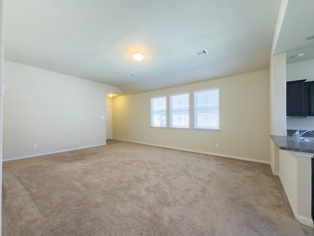 unfurnished living room featuring light colored carpet, visible vents, a sink, and baseboards