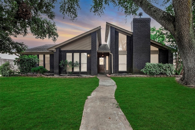 mid-century modern home with a chimney, a lawn, and brick siding