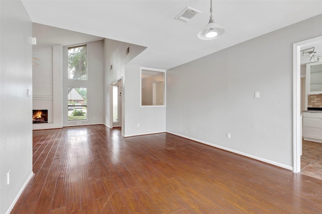 unfurnished living room featuring wood-type flooring, visible vents, a towering ceiling, a brick fireplace, and baseboards