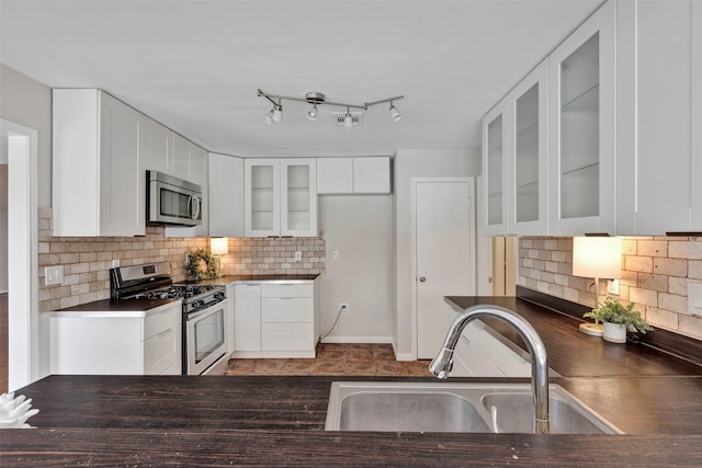 kitchen featuring dark countertops, white cabinets, stainless steel appliances, and a sink