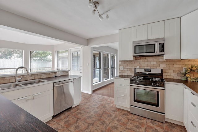 kitchen with dark countertops, backsplash, appliances with stainless steel finishes, white cabinets, and a sink