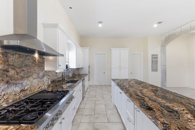 kitchen with tasteful backsplash, dark stone countertops, stainless steel appliances, wall chimney range hood, and a sink