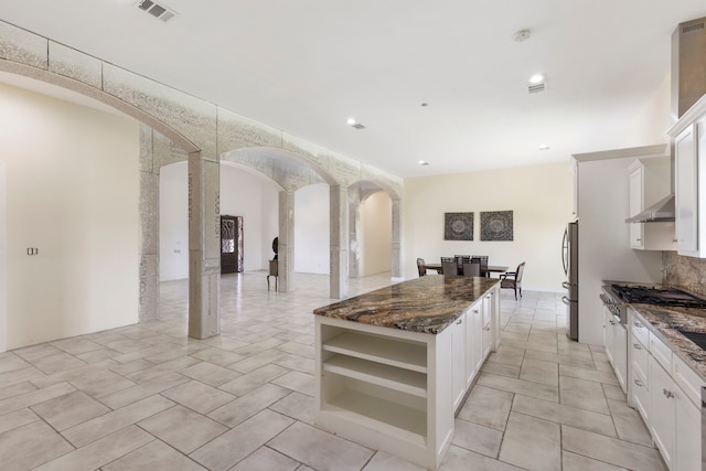 kitchen featuring arched walkways, visible vents, freestanding refrigerator, a kitchen island, and dark stone counters