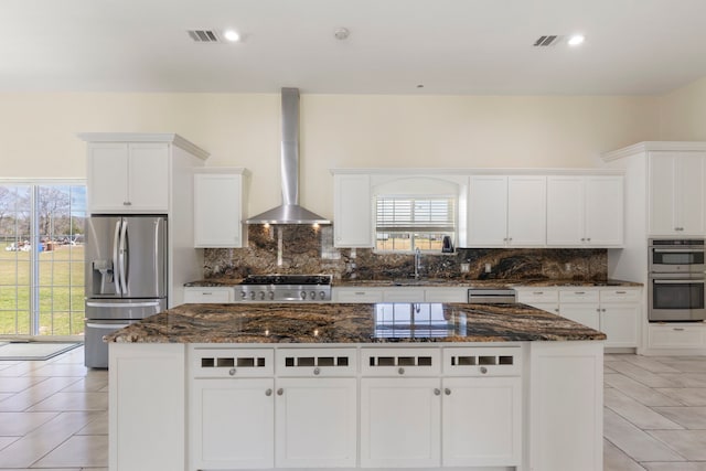 kitchen featuring tasteful backsplash, visible vents, wall chimney exhaust hood, appliances with stainless steel finishes, and a sink