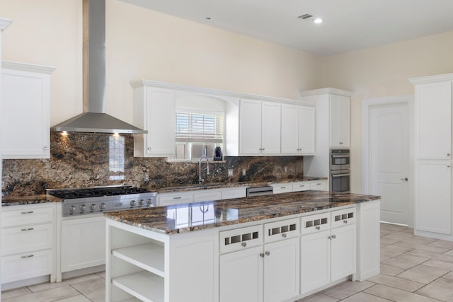 kitchen featuring dark stone countertops, stainless steel appliances, wall chimney range hood, white cabinetry, and backsplash