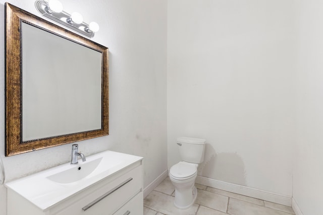 half bathroom featuring toilet, vanity, baseboards, and tile patterned floors