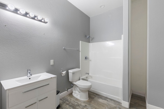 bathroom with a textured wall, toilet, wood finished floors, vanity, and shower / bathing tub combination