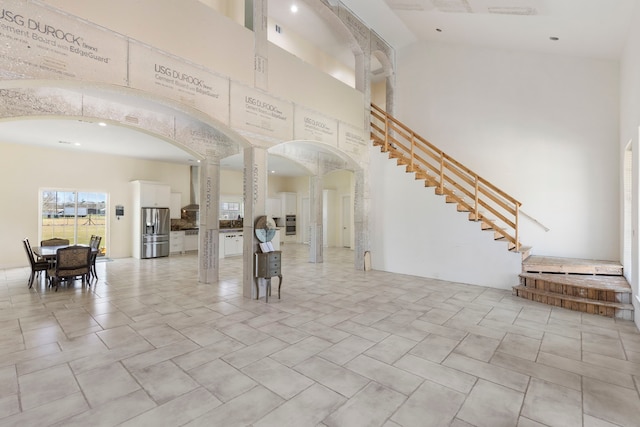 foyer entrance featuring arched walkways, a high ceiling, stairs, and decorative columns