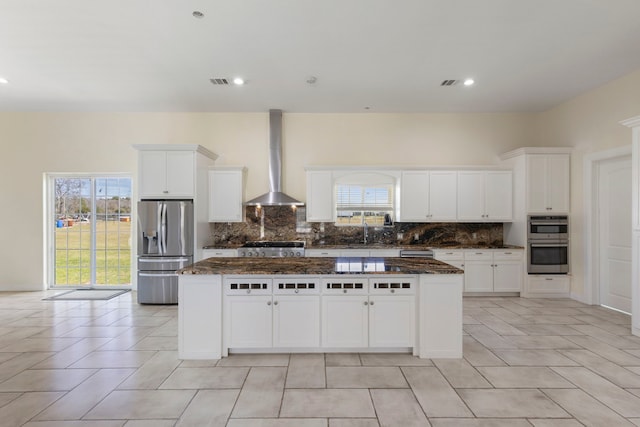 kitchen featuring a sink, a kitchen island, appliances with stainless steel finishes, backsplash, and wall chimney exhaust hood