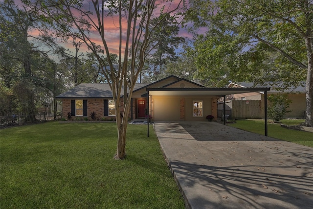 view of front facade with concrete driveway, an attached carport, fence, a front lawn, and brick siding