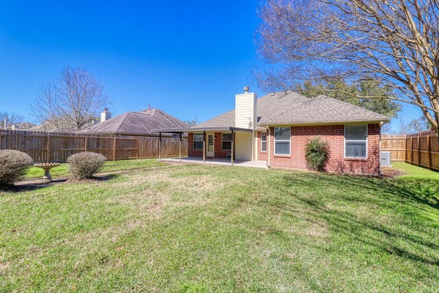 back of house featuring a patio, a yard, a fenced backyard, a chimney, and brick siding