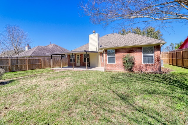 back of house featuring brick siding, a chimney, a fenced backyard, a yard, and a patio area