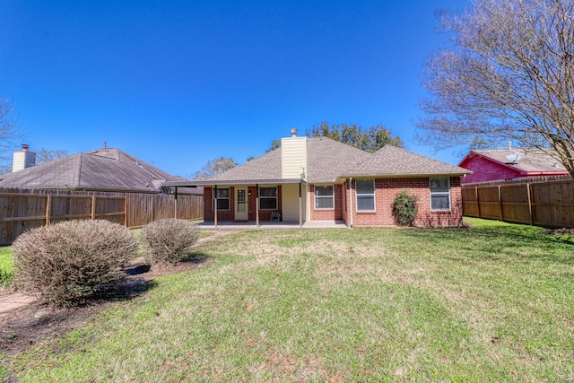 back of house featuring a yard, a fenced backyard, a chimney, a patio area, and brick siding