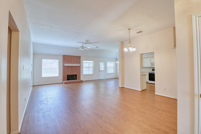 unfurnished living room featuring visible vents, ceiling fan with notable chandelier, a fireplace, light wood finished floors, and baseboards