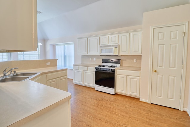 kitchen with white microwave, a sink, light countertops, light wood-style floors, and gas range