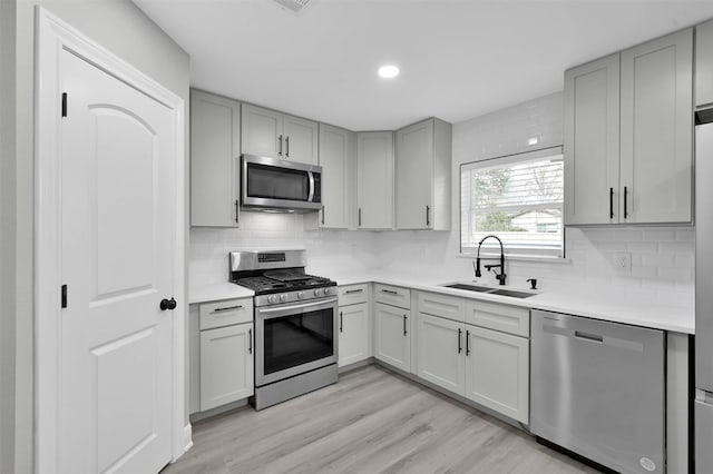 kitchen featuring light countertops, appliances with stainless steel finishes, a sink, and gray cabinetry