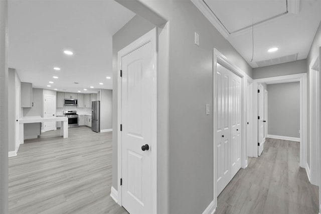 hall with attic access, baseboards, light wood-style flooring, and recessed lighting