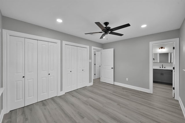 unfurnished bedroom with two closets, recessed lighting, a sink, light wood-type flooring, and baseboards