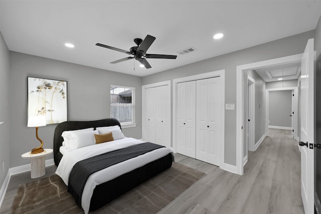 bedroom featuring light wood-type flooring, attic access, baseboards, and multiple closets