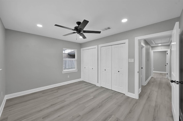 unfurnished bedroom featuring baseboards, two closets, attic access, and light wood-style floors