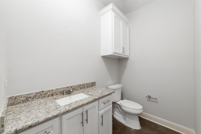 half bathroom with toilet, wood finished floors, vanity, and baseboards