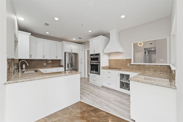 kitchen with light stone counters, a sink, visible vents, appliances with stainless steel finishes, and custom range hood
