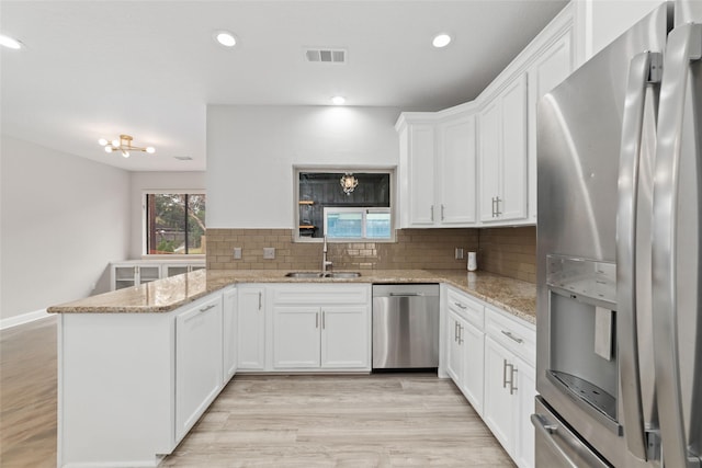 kitchen with visible vents, appliances with stainless steel finishes, a peninsula, a sink, and backsplash
