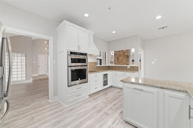 kitchen with stainless steel appliances, visible vents, light wood-style flooring, decorative backsplash, and white cabinets