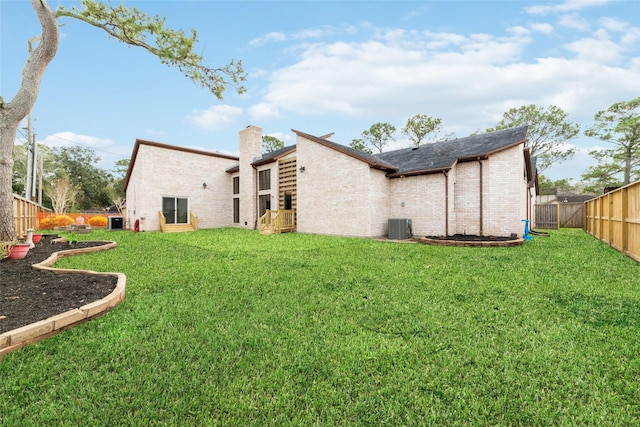 back of property featuring a fenced backyard, a yard, a chimney, and brick siding