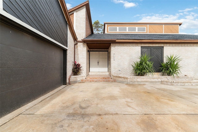 exterior space featuring a garage, concrete driveway, brick siding, and a patio