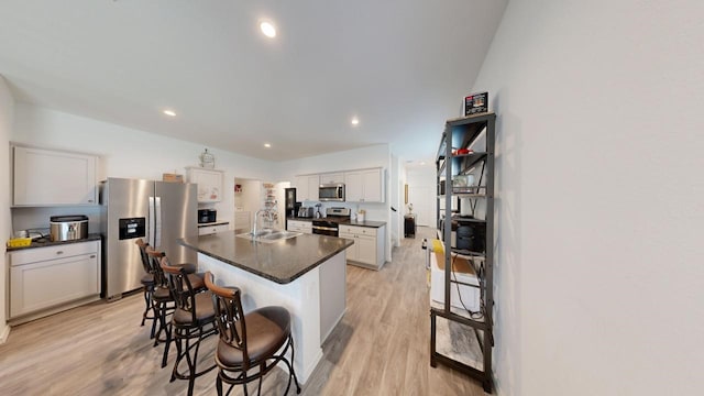 kitchen featuring stainless steel appliances, dark countertops, light wood-style floors, and a sink