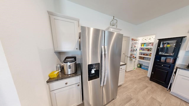 kitchen featuring white cabinets, stainless steel fridge, and dark stone countertops