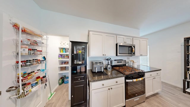 kitchen featuring baseboards, white cabinets, appliances with stainless steel finishes, dark stone countertops, and light wood-type flooring