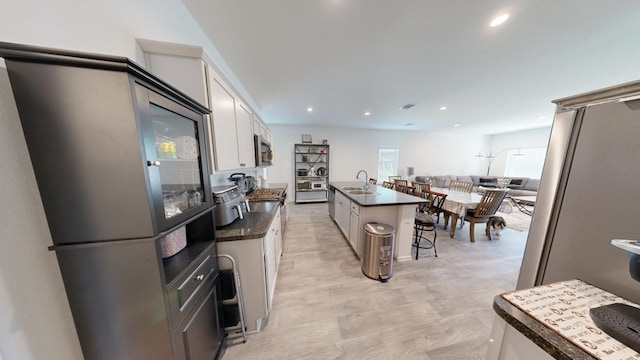 kitchen with white cabinets, dark countertops, appliances with stainless steel finishes, open floor plan, and a sink